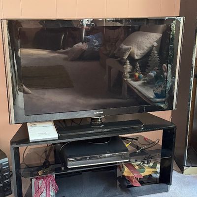 Samsung flat-screen television with stand, accompanied by a media player on a black glass and metal entertainment console.