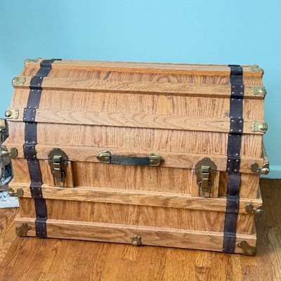 Vintage dome-top wooden steamer trunk with brass hardware and dark leather straps.