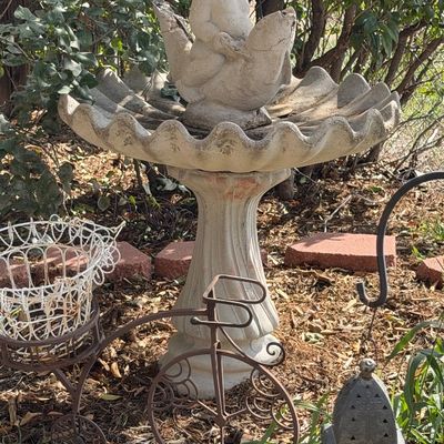Concrete garden fountain with a child riding a fish topper, paired with a metal tricycle plant stand and a decorative lantern in a yard...