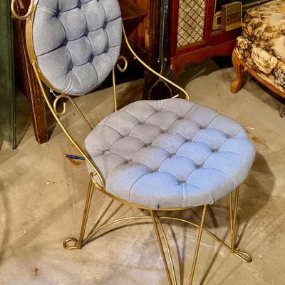Mid-century Hollywood Regency style vanity chair with a scrollwork brass frame and tufted round cushions in light blue fabric.
