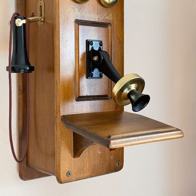 Vintage-style 'The Country Belle' wooden wall-mounted telephone featuring brass ringer bells and a classic earpiece, in good...
