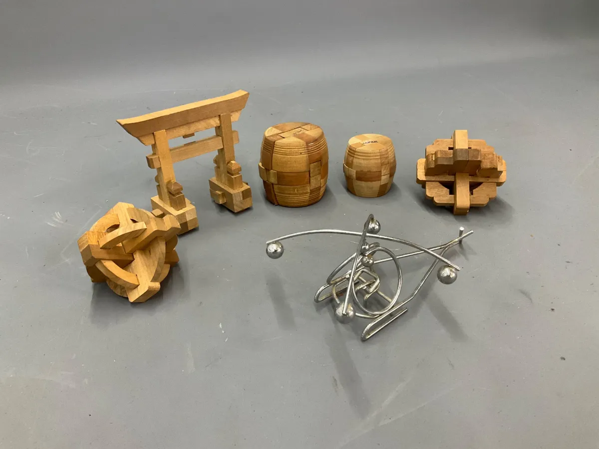 Sale Photo Thumbnail #343: Collection of vintage mechanical brain teaser puzzles, including wooden kumiki interlocking shapes, barrel puzzles, a Japanese torii gate puzzle, and metal wire tavern puzzles.