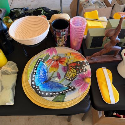 Sale Photo Thumbnail #155: Assortment of household goods, including a decorative glass butterfly plate, carved wooden yoga figurine, Taylor Swift tumbler, white ceramic pitcher, and bread proofing basket.