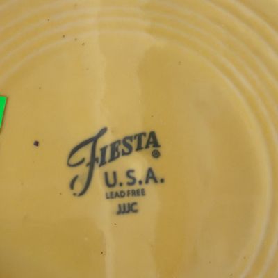 Sale Photo Thumbnail #162: Underside maker's mark on a yellow Fiesta lead-free ceramic dish, displaying the stamped logo and concentric ring pattern.