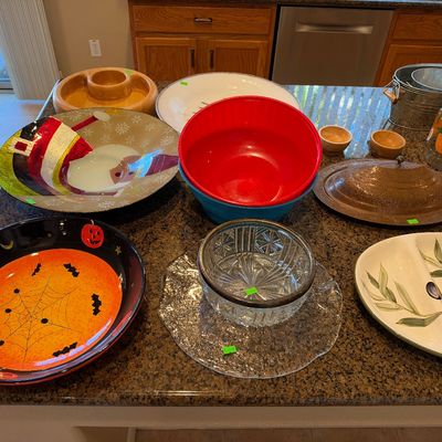 An assortment of servingware and decorative bowls arranged on a granite countertop, including holiday-themed ceramic dishes, Pyrex or...