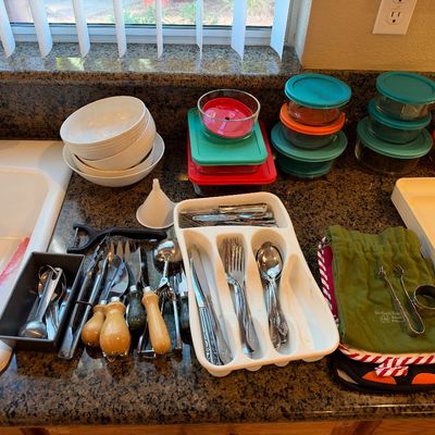Collection of kitchen items including Pyrex glass food storage containers with colorful lids, white ceramic bowls, stainless steel...