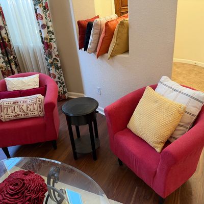 Pair of contemporary bright red tub armchairs styled with accent pillows, flanked by a small black round side table.