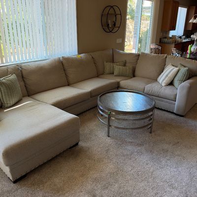 Large beige sectional sofa with nailhead trim and chaise lounge, paired with a round metal coffee table.