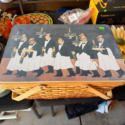 Sale Photo Thumbnail #165: Vintage woven picnic basket featuring a wooden lid decorated with an illustration of waiters carrying champagne.