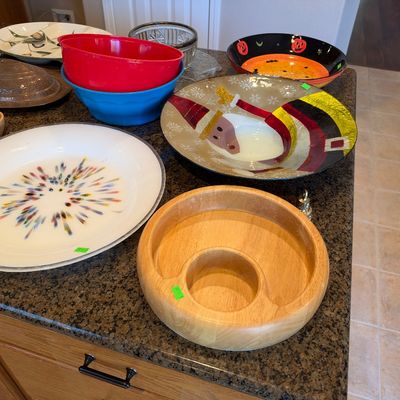 Collection of decorative serving platters and bowls, including a wooden chip-and-dip tray, colorful glass dishes, festive holiday...