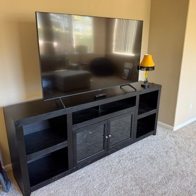 Black wooden media console console table supporting a modern flat-screen television with remote control.