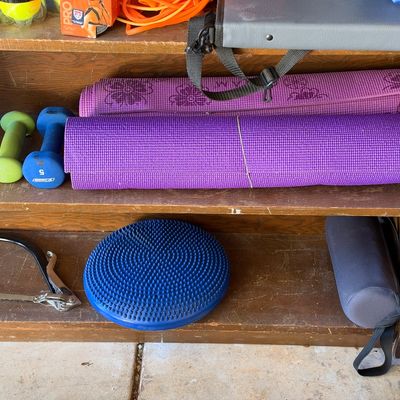 Sale Photo Thumbnail #147: Wooden storage shelves featuring various exercise equipment, including rolled yoga mats, small dumbbells, a blue balance disc, and a bow saw.