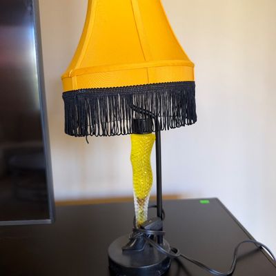 Novelty leg lamp inspired by 'A Christmas Story', featuring a yellow fabric shade with black fringe trim.