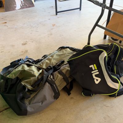 Large green and grey hiking duffel bag alongside a black and neon green Fila duffel bag resting on a garage floor.