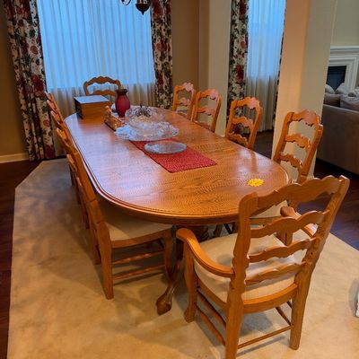 Traditional oak dining room set featuring an oval pedestal dining table and ten ladder-back chairs with cushioned seats.