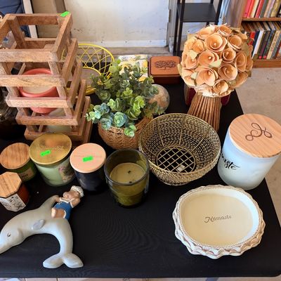 Sale Photo Thumbnail #158: Collection of home decor items including scented candles in glass jars, a wooden open-frame lantern, artificial topiary plants, and a porcelain dolphin figurine.