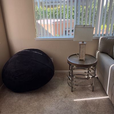 Large black suede beanbag chair alongside a contemporary metal and wood end table with a small table lamp.