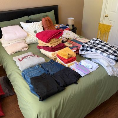Assortment of household linens, folded bath towels, throw blankets, and folded clothing laid out on a bed.