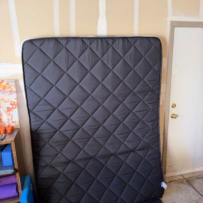 Sale Photo Thumbnail #137: Black quilted mattress leaning vertically against an unfinished wall.