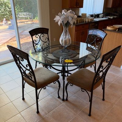 5-piece dining set featuring a round glass-top table with wrought iron base and four matching scrolled metal chairs with beige...