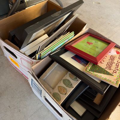 Two cardboard boxes packed with assorted modern picture frames, holiday art prints, and decorative plaques.