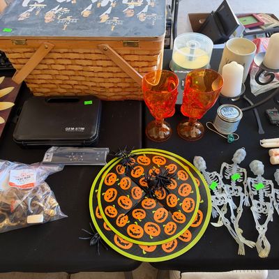 Sale Photo Thumbnail #152: Collection of Halloween decor, including orange skull goblets, plastic skeleton figures, pumpkin placemats, alongside candles, a picnic basket, and household items.