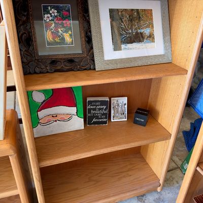 Sale Photo Thumbnail #105: Light oak bookcase displaying framed artwork, including a Santa painting and small decorative block signs.