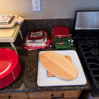 Selection of kitchen and holiday tableware including stacked red charger plates, wooden serving trays, and folded festive kitchen towels...