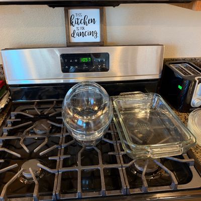 Selection of clear glass kitchenware including Pyrex baking dishes, mixing bowls, and plates sitting on a gas stove stovetop.