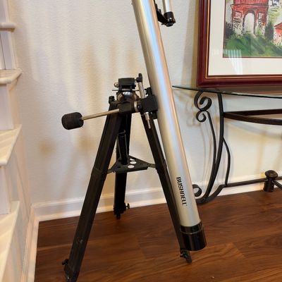 Bushnell refractor telescope with silver tube, finderscope, and adjustable black wooden tripod.