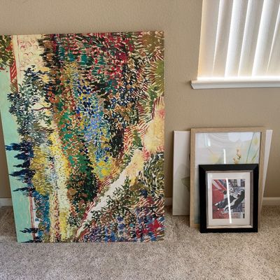 Large unframed canvas art print featuring a colorful pointillist garden landscape, leaning against a wall alongside smaller framed prints.