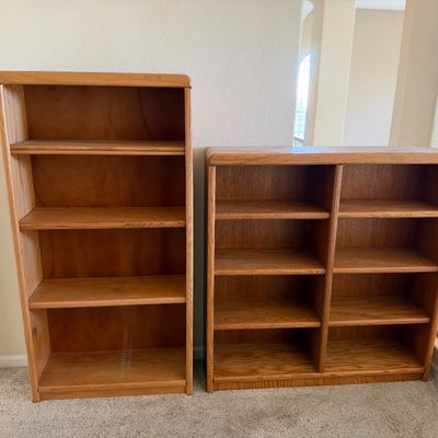 Pair of light oak wooden bookcases, including one tall four-shelf unit and one wide double-column unit with rounded top edges.