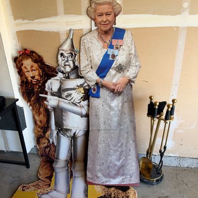 Sale Photo Thumbnail #117: Life-size cardboard cutouts of Queen Elizabeth II in formal regalia alongside the Cowardly Lion and Tin Man from The Wizard of Oz, accompanied by a brass fireplace tool set.