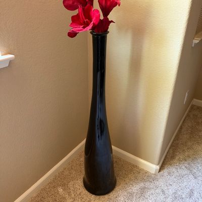Tall glossy black ceramic floor vase holding a cluster of faux red amaryllis blooms.