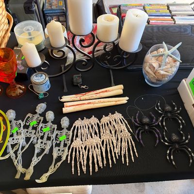 Sale Photo Thumbnail #151: Collection of Halloween decorations including skeleton figures, glitter spiders, bleeding taper candles, a wrought iron candelabra with pillar candles, and amber glassware.