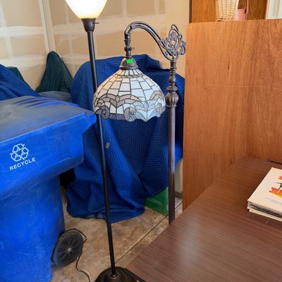 Two floor lamps, including a modern torchiere lamp and a Tiffany-style stained glass bridge arm floor lamp with decorative metalwork.