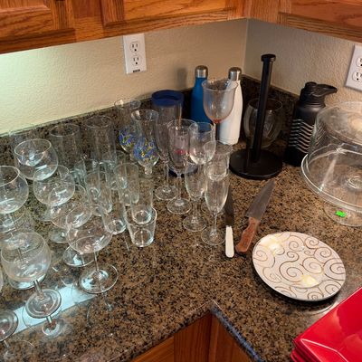 Collection of kitchen and glassware items including wine glasses, tumblers, a glass cake dome, knives, and decorative plates.