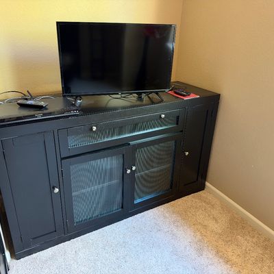 Black wooden media console with ribbed glass door panels, topped with a flat-screen television and a Panasonic Blu-ray player.