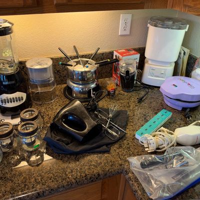 Assortment of small kitchen appliances on a countertop, including a Black & Decker blender, an Oster food processor, a fondue pot,...