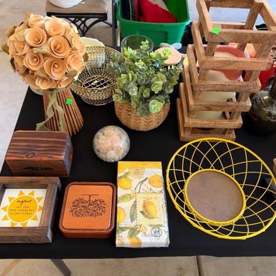 Sale Photo Thumbnail #157: A table filled with home decor items including faux floral arrangements, wooden boxes, a yellow wire basket, and various tabletop accents.