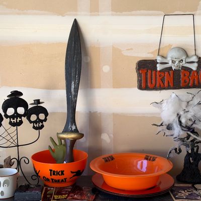 Sale Photo Thumbnail #141: Collection of Halloween decorations including an orange trick-or-treat bowl, a prop sword, a skull candelabra, and a hanging "Turn Back!" sign.