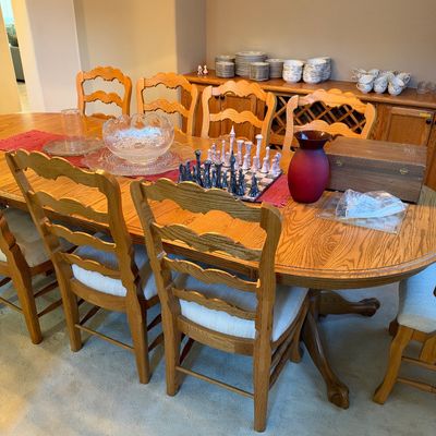 Large light oak dining table with pedestal feet and ladderback chairs, displayed alongside crystal serveware, a decorative chess set, and...