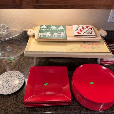 Collection of holiday kitchenware and serving items, including red ceramic dinnerware, a glass cake stand dome, decorated wooden trays,...