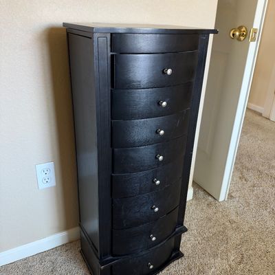 Sale Photo Thumbnail #101: Black wooden standing jewelry armoire featuring curved drawer fronts with silver-tone knobs.