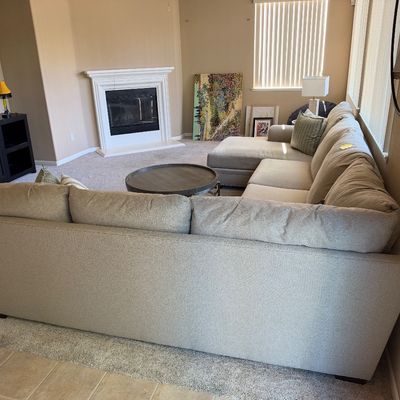 Contemporary beige upholstered sectional sofa with chaise and accent pillows, paired with a round wooden coffee table in a living room...