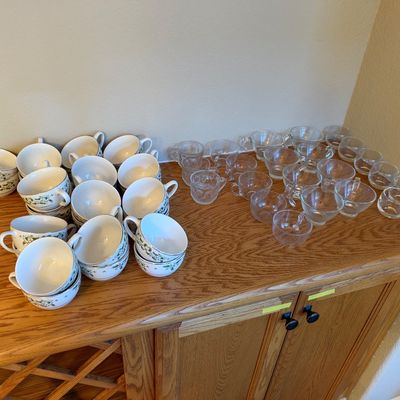 Collection of vintage china teacups with green ivy motif alongside assorted clear glass teacups and punch cups, displayed on an oak...