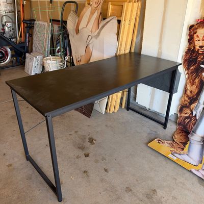 Sale Photo Thumbnail #115: Modern dark brown writing desk with a black metal frame, shown alongside cardboard cutouts in a garage storage space.