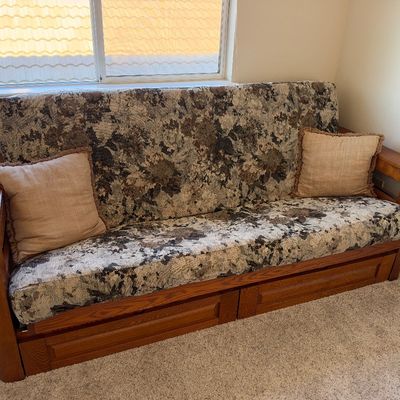 Wooden frame futon with patterned tapestry upholstery, under-seat storage drawers, and two beige throw pillows.
