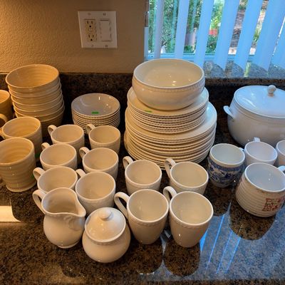 Large collection of white and beige ceramic dinnerware, including stacks of plates, bowls, coffee mugs, a creamer, sugar bowl, and a...