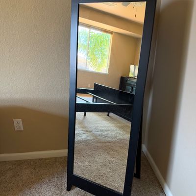 Sale Photo Thumbnail #103: Modern black wood freestanding cheval mirror with an arched top, set in the corner of a carpeted room.